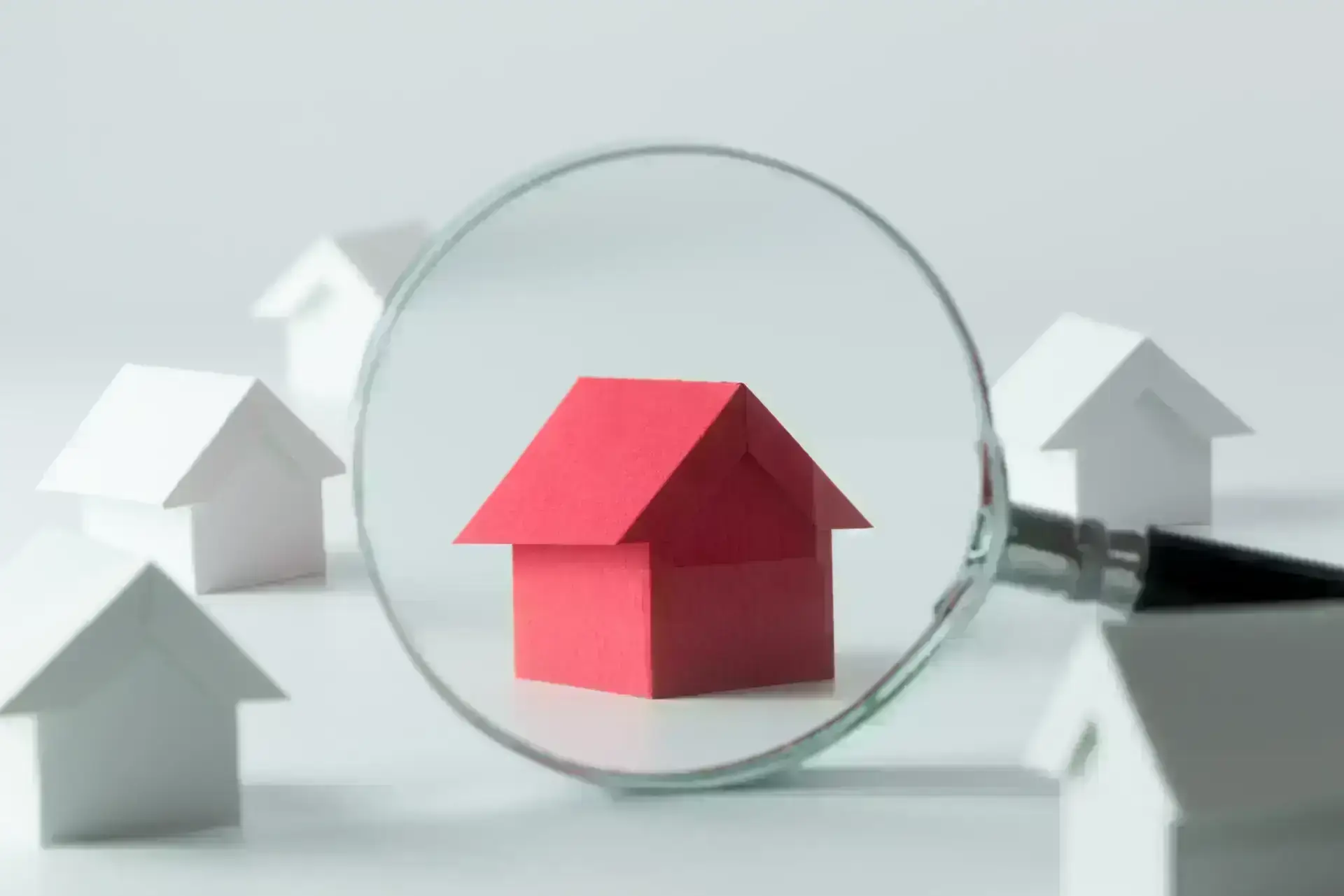 magnifying glass over red house model, white houses in background