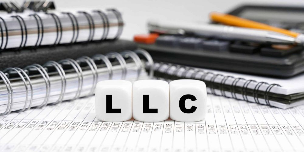 LLC spelled out on dice on top of spreadsheet beside notebooks