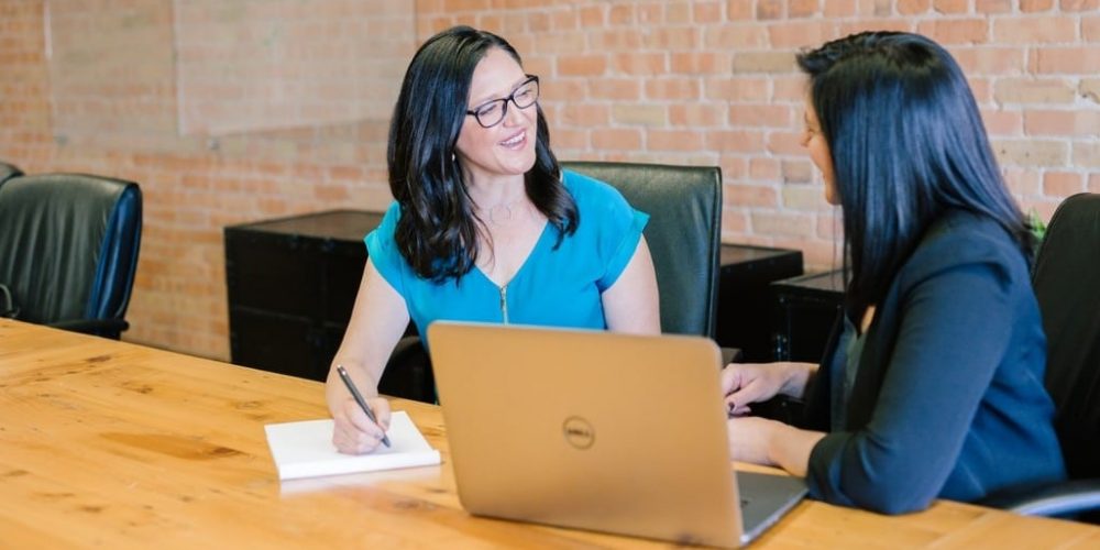 two women talking in front of a computer