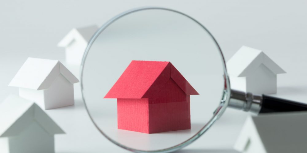magnifying glass over red house model, white houses in background